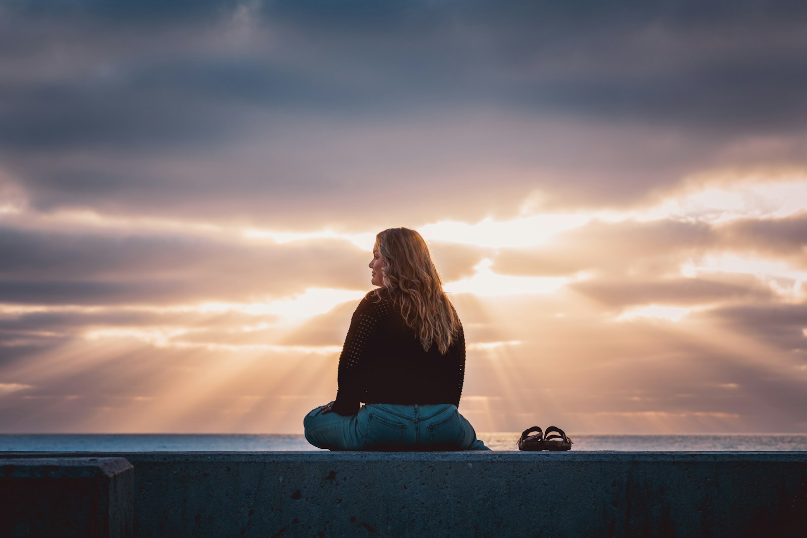 A woman sitting on a wall looking at the sky